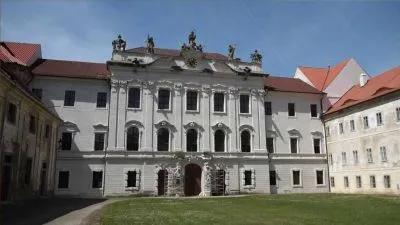 Fasáda kláštera v Broumově s červenou střechou na zelené trávě.