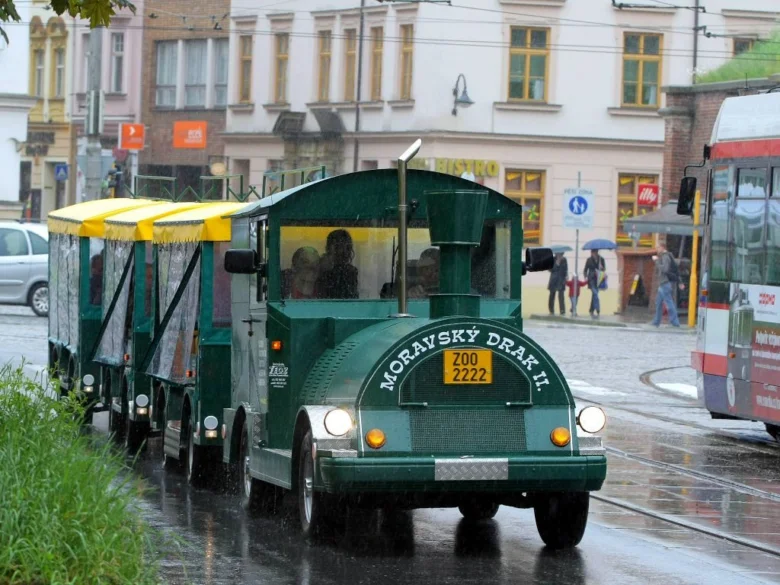 Zelený turistický vláček jezdí po mokré ulici v dešti.