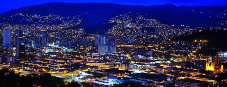 Noční pohled na město Medellín s osvětlenými budovami v horách.