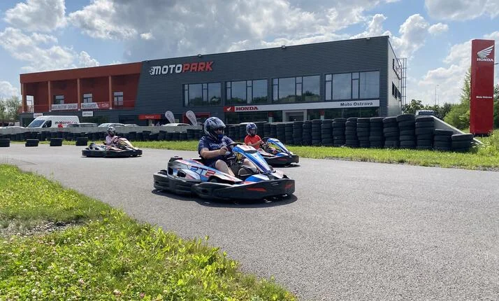 Tři lidé jezdí motokáry na okruhu před budovou MOTOPARK.