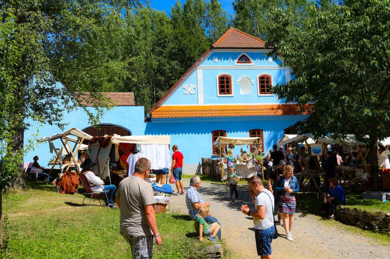 Venkovní trh s stánky před modrou budovou na slunečním dni.