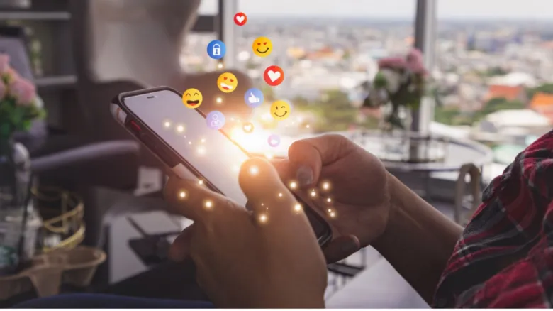 Osoba drží chytrý telefon s vysílanými smajlíky na pozadí města.