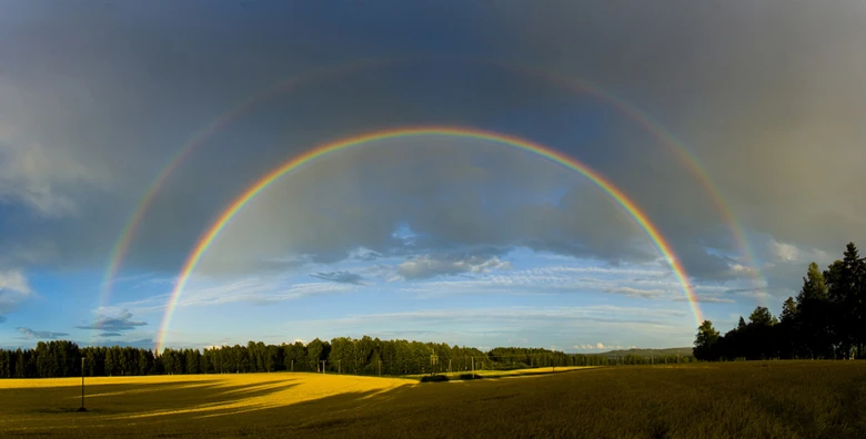 Dvojitá duha s plným pořadím barev nad poli.