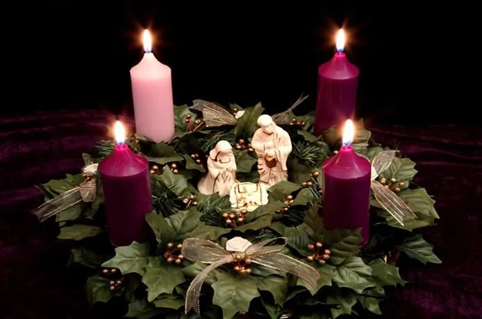 Adventní věnec s rozsvícenými svíčkami a betlémskou scénou.