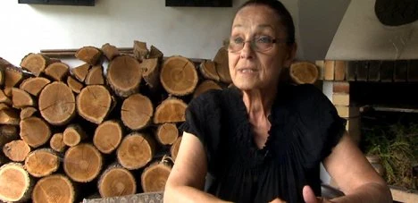 Žena sedí před hromadou dřeva v interiéru.