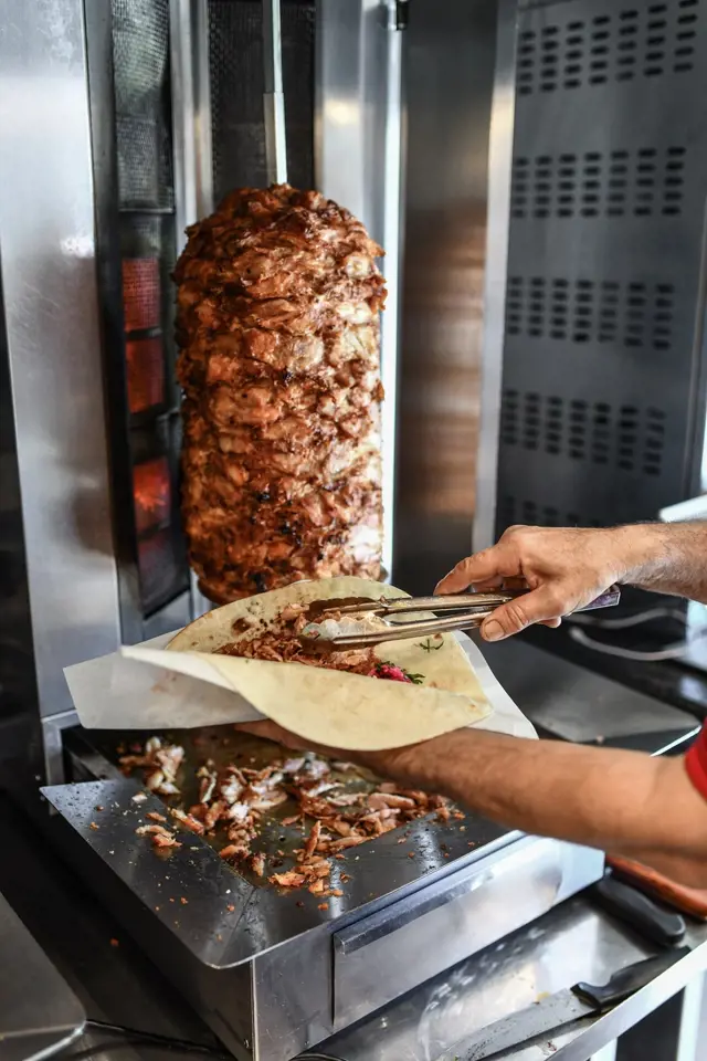 Kuchař krájí kebab z vertikálního grilu na placku.