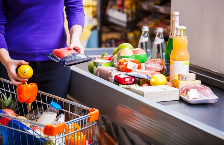 Kupující v supermarketu s košíkem plným ovoce a zeleniny na pokladně.