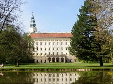 Zámek v Kroměříži s parkem a odrazem ve vodní ploše.