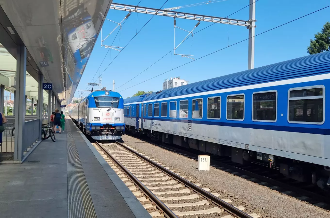 Modro-bílý vlak na nádraží v Praze Vršovicích s cestujícími