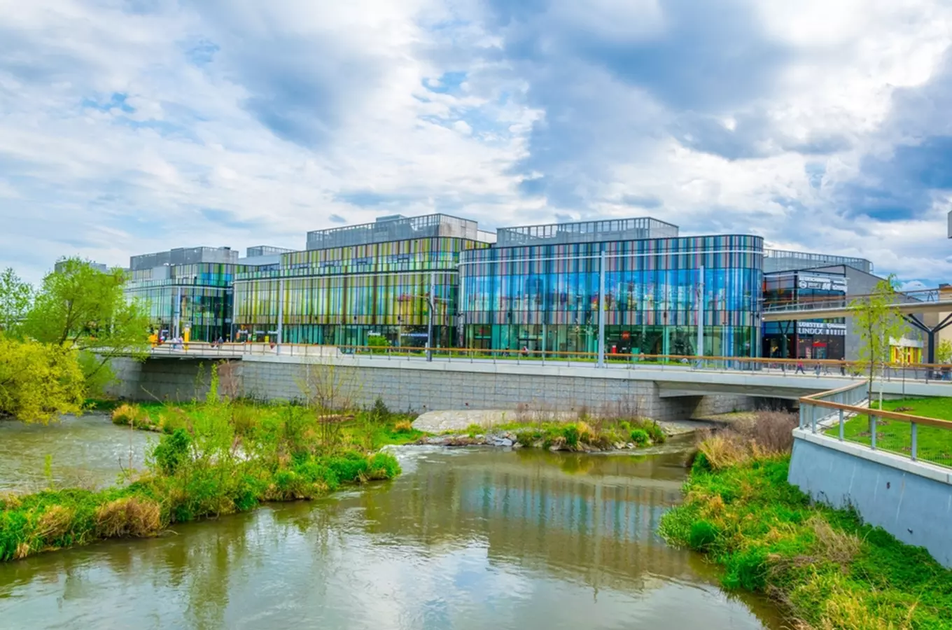 Exteriér nákupního centra Šantovka v Olomouci s řekou před budovou.