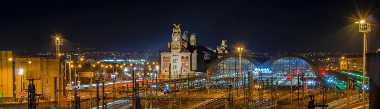 Noční pohled na hlavní nádraží v Praze s osvětlenými kolejemi.