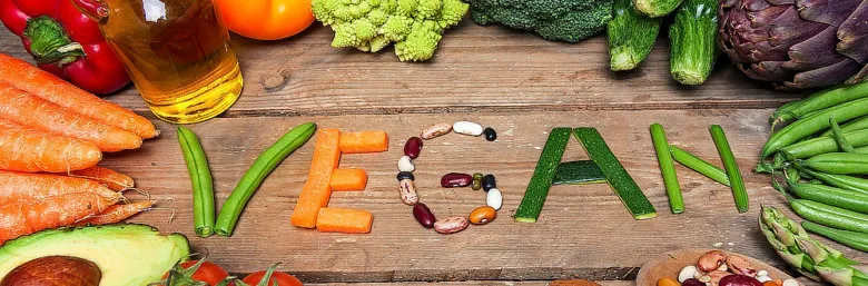 Různé čerstvé zeleniny a ovoce tvořící slovo VEGAN na dřevě.