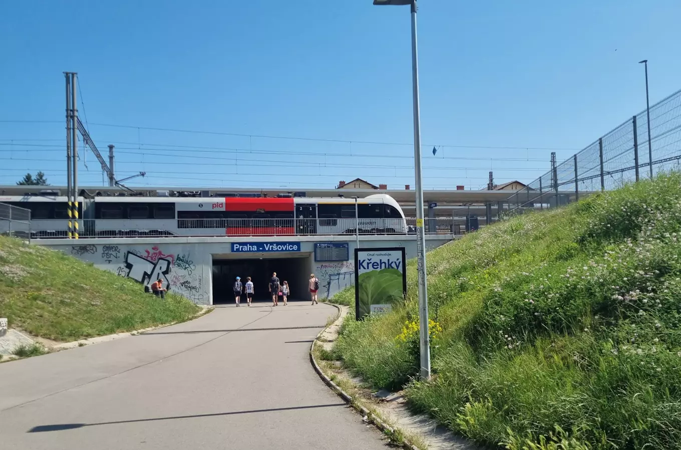 Vstup do stanice Praha-Vršovice s vlakem nad podjezdem.
