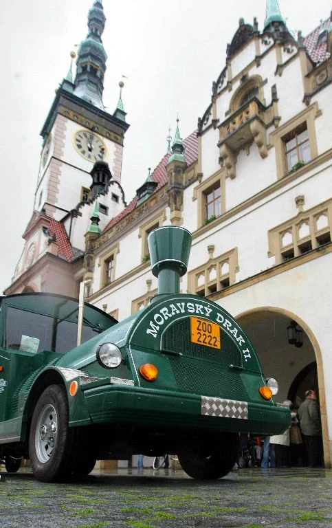 Zelený turistický vlak před historickou budovou v centru města.