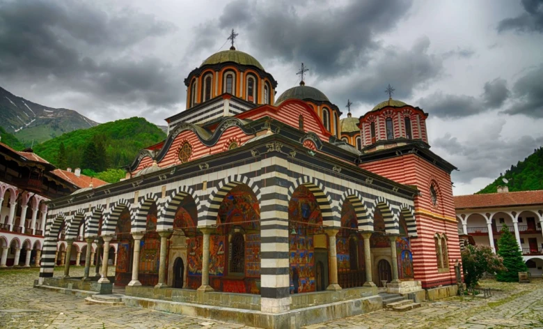 Historický bulharský klášter s klenutými arkádami na pozadí hor.