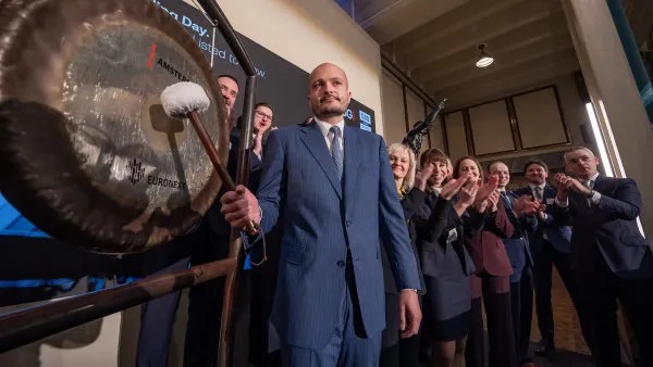 Muž v obleku buší do velkého kovu, zatímco ostatní aplaudují.