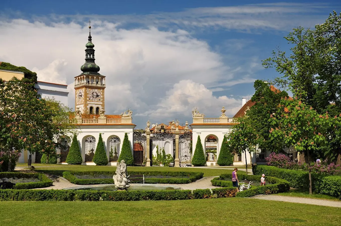 Zahrada zámku Mikulov s fontánou, sochami a návštěvníky na chodbách.