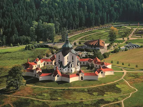 Zámek s červenými střechami v zeleném parku uprostřed lesa.