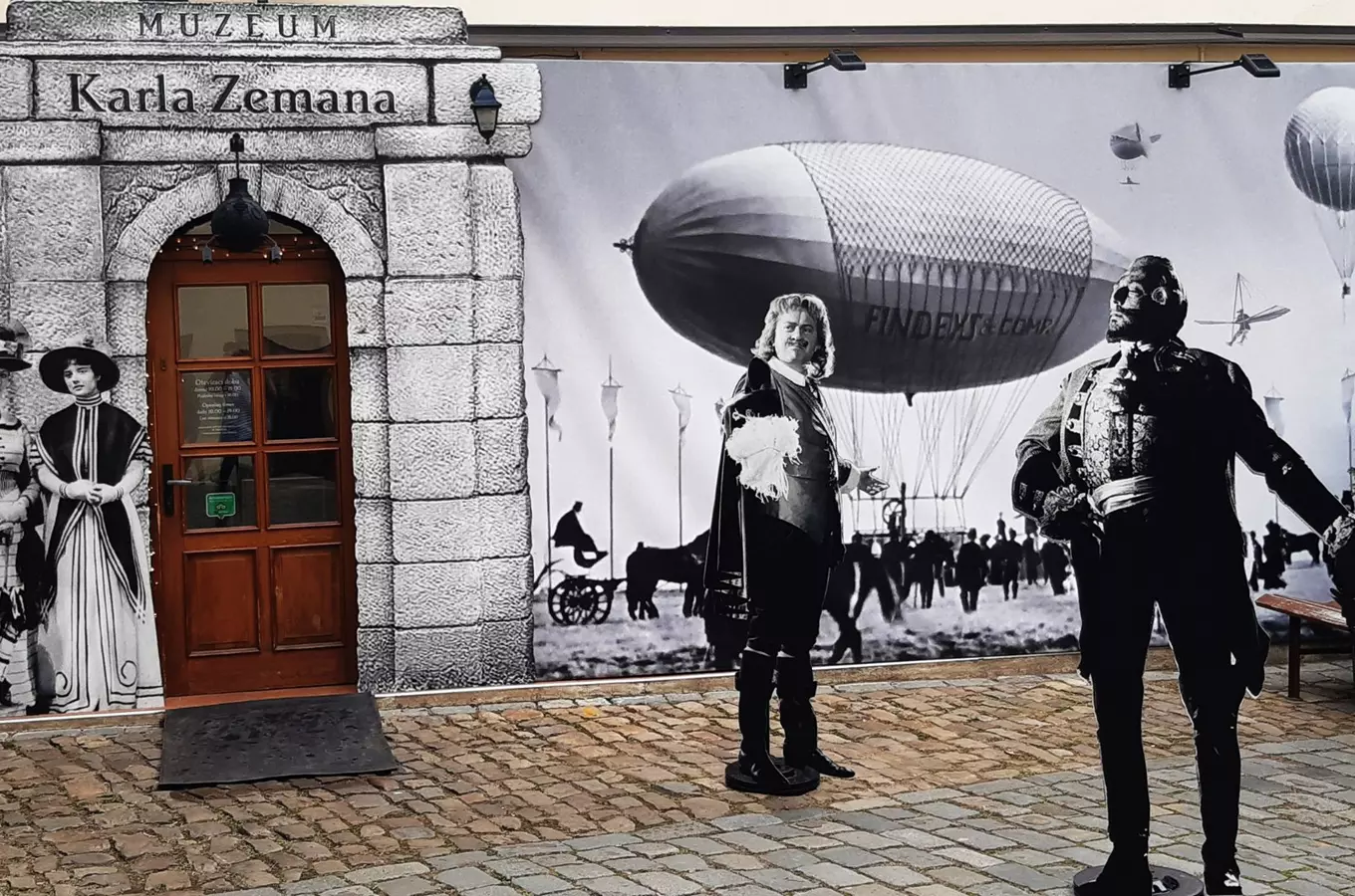 Vstup do muzea s výstřihy postav před historickou grafikou.