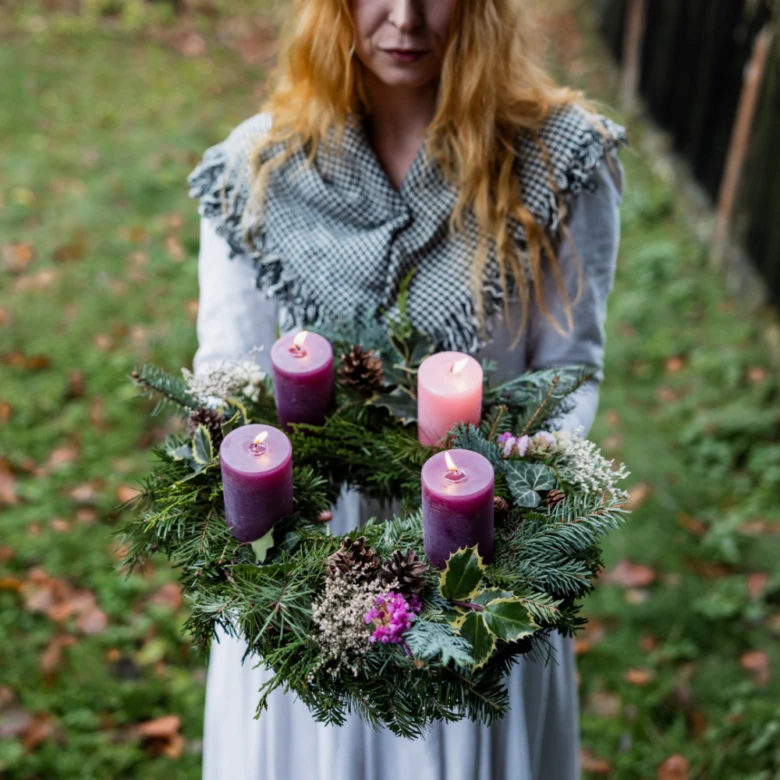 Žena drží adventní věnec se svíčkami venku.