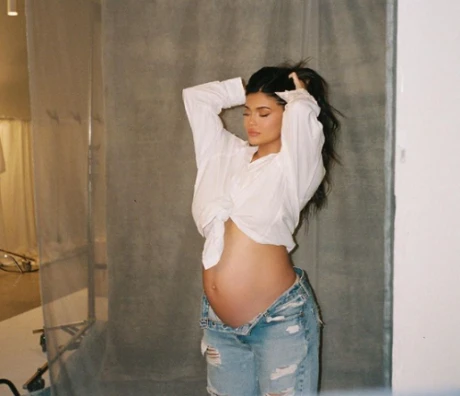 Těhotná Kylie Jenner v bílé košili s odhaleným břichem.