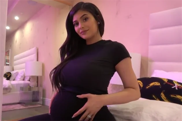 Těhotná Kylie Jenner v ložnici drží ruku na břiše.