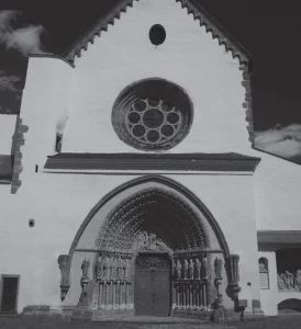 Fotografie gotického kostela s okrouhlým okenem a zdobenou bránou.