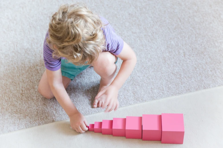 Dítě hraje s růžovými dřevěnými kostkami podle montessori metody.