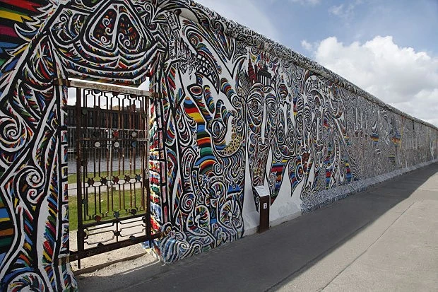 Zdi berlínské zdi s barevnými grafiti pod modrou oblohou.