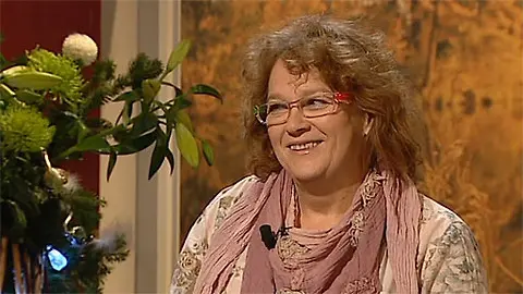 Žena s brýlemi a šátkem na pozadí v interiéru.