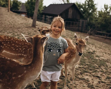 Dívka stojí mezi dvěma jeleny v přírodním prostředí.