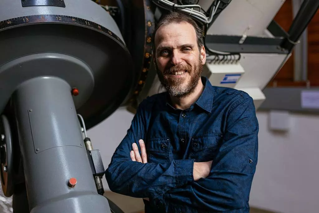 Muž stojí vedle velkého astronomického dalekohledu.
