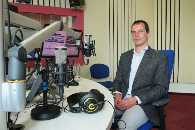Muž sedí v rozhlasové studii s mikrofony a sluchátky.