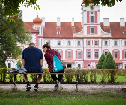 Dvojice sedí na lavičce před zámek v parku Lednice.