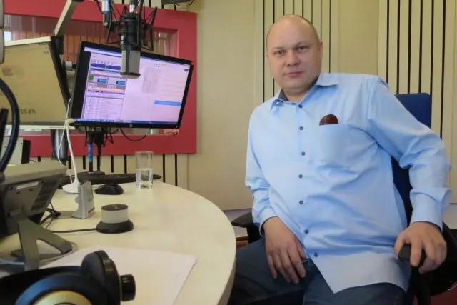 Muž sedí v rozhlasové studii s mikrofony a monitory.