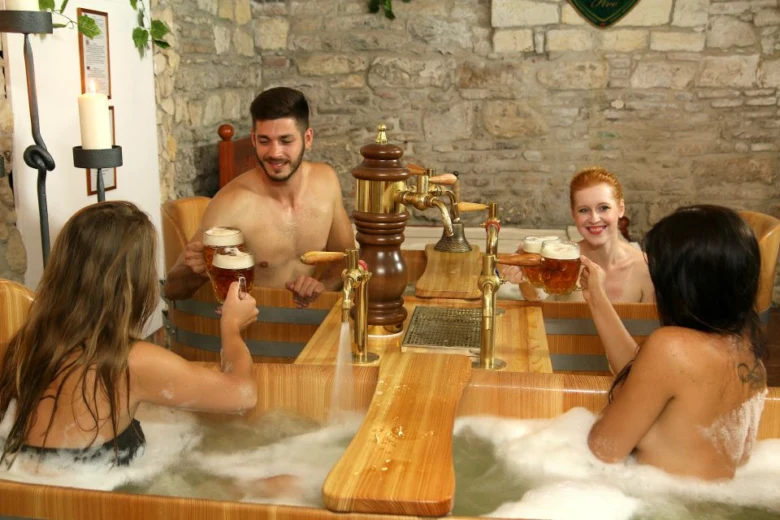 Lidé relaxují v dřevěné vaně s pivem ve wellness centru.