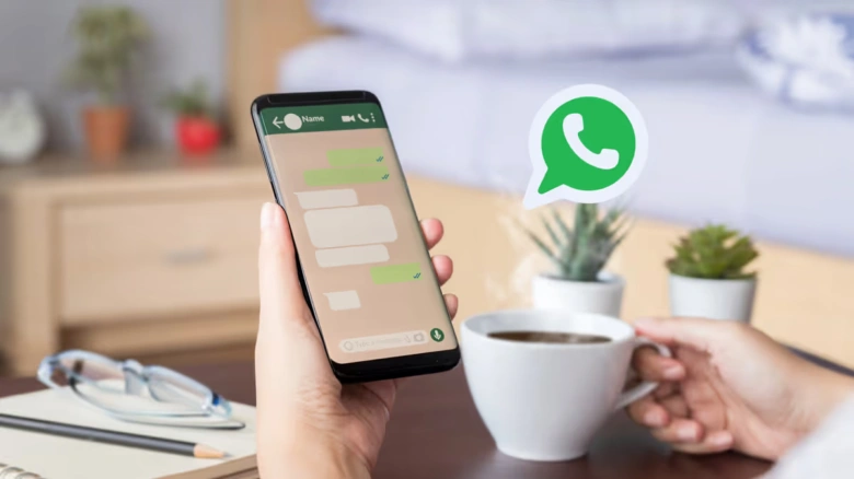 Ruka drží chytrý telefon s aplikací WhatsApp při pití kávy.