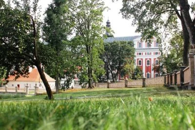 Kostel s červenými zdmi v klášterním areálu mezi stromy.