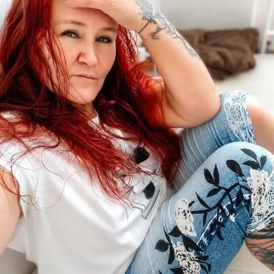 Žena s červenými vlasy se dívá na kameru v interiéru.