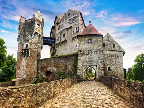 Starý hrad s mostem a věžemi na pozadí modré oblohy.