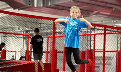 Dívka skáče na trampoline v areálu s bezpečnostními síťemi.