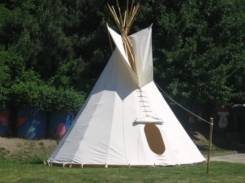 Bílé dětské teepee stojí na trávníku před stromy.