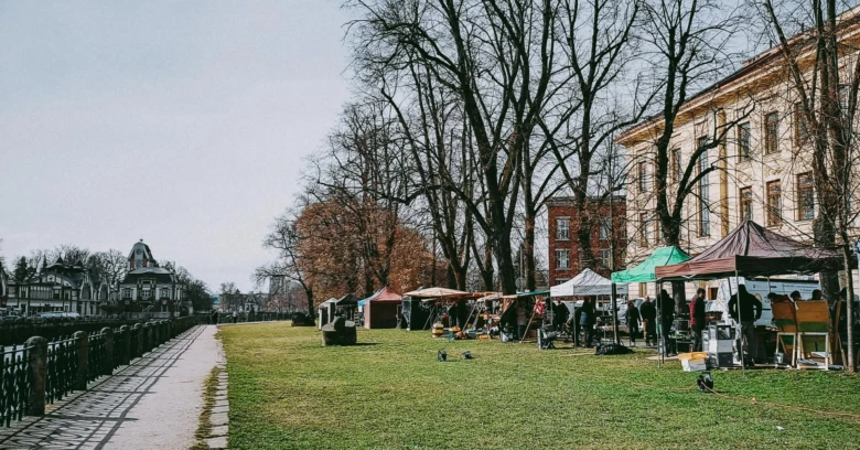 Venkovní trh s stánky na trávníku v parku u řeky.