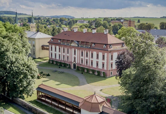 Historické zámek v Raduni s okolní zelení a menšími budovami.