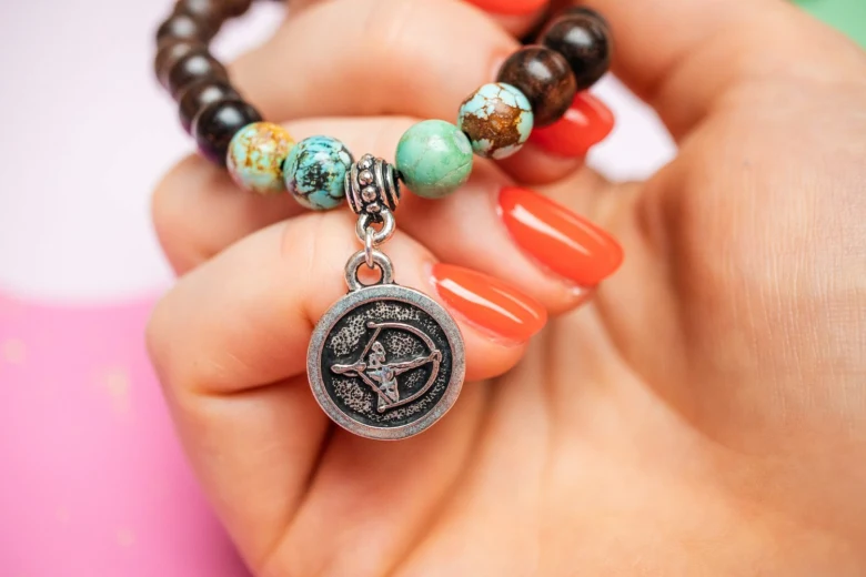 Rukou drží náramek s amuletem znamení Zvěrokruhu Střelec.