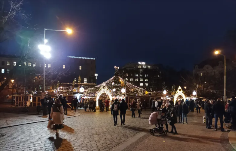 Vánoční trh na náměstí Míru v Praze za tmy s lidmi a osvětlenými stánky.