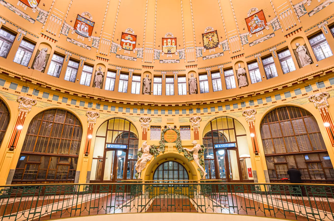 Vnitřní hala hlavního nádraží v Praze s architektonickými detaily a sochami.