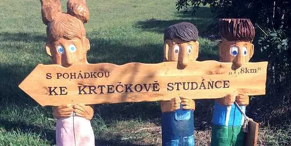 Dřevěný ukazatel s sochami směřující k Krtečkovu studánce.