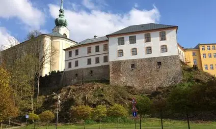 Zámek v Trutnově na kopci s věží pod modrou oblohou.