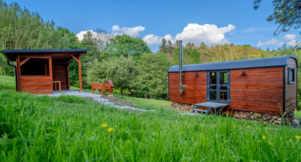 Dva dřevěné ubytovací chatky pro glamping na trávnaté svahu.